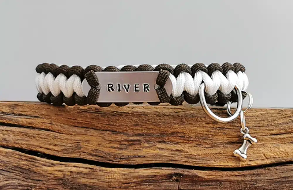 A handmade dog collar braided with paracord 550 in the cobra knot style and a metal tag displaying dogs name 'RIVER'